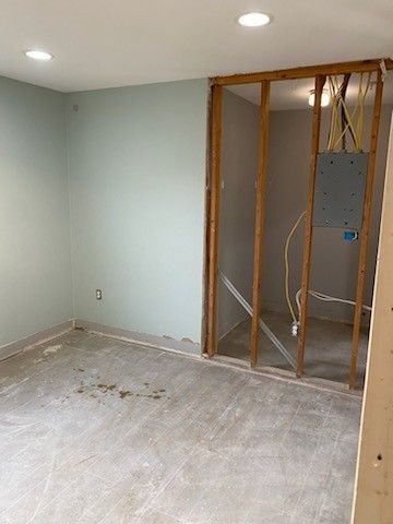 A room under renovation with a sage green finished wall next to an open wooden stud frame containing an electrical panel.
