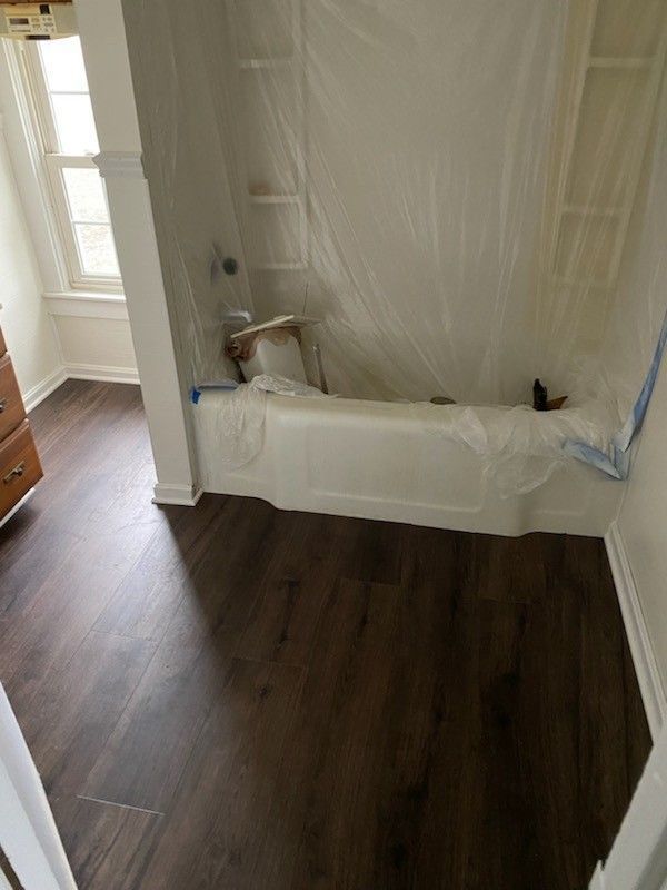 A bathroom with dark wood-look flooring and a bathtub covered in protective plastic sheeting during a renovation.