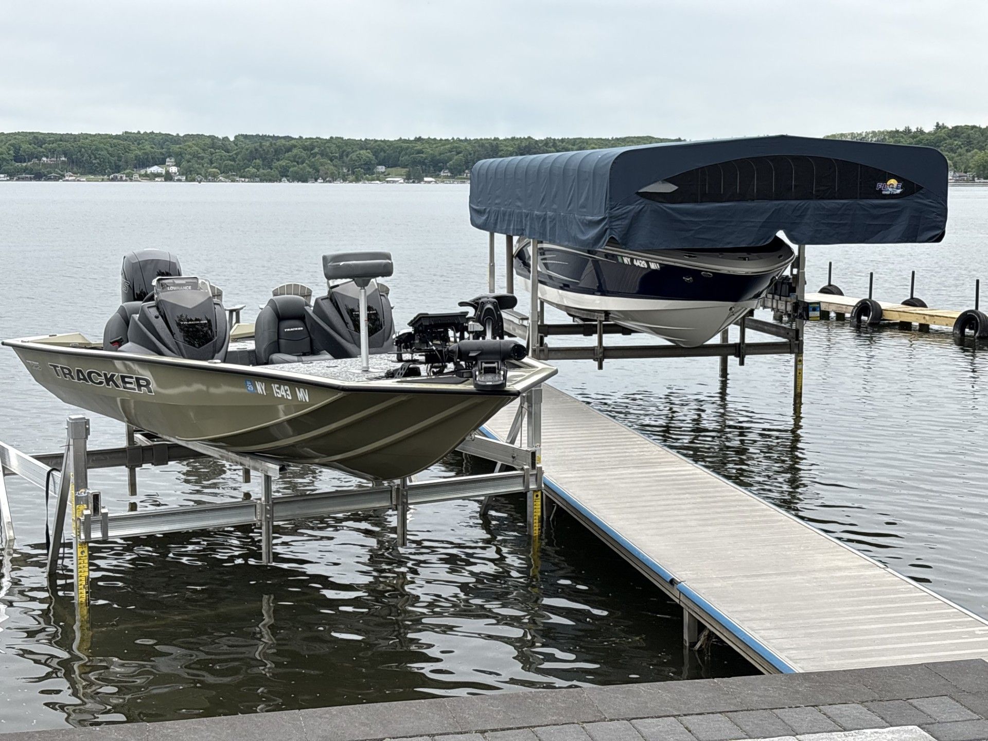 Motorboat docked beside a wooden pier on a calm lake, with a covered boat on a lift nearby.