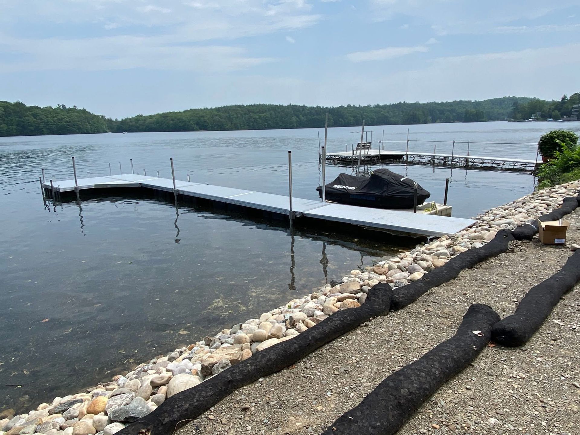 A long floating dock extends into a calm lake from a rocky shoreline, with a small covered boat moored beside it.