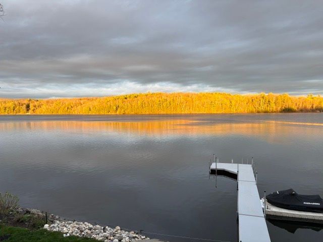 Calm lake at sunset with golden trees on the far shore and a dock with a boat in the foreground
