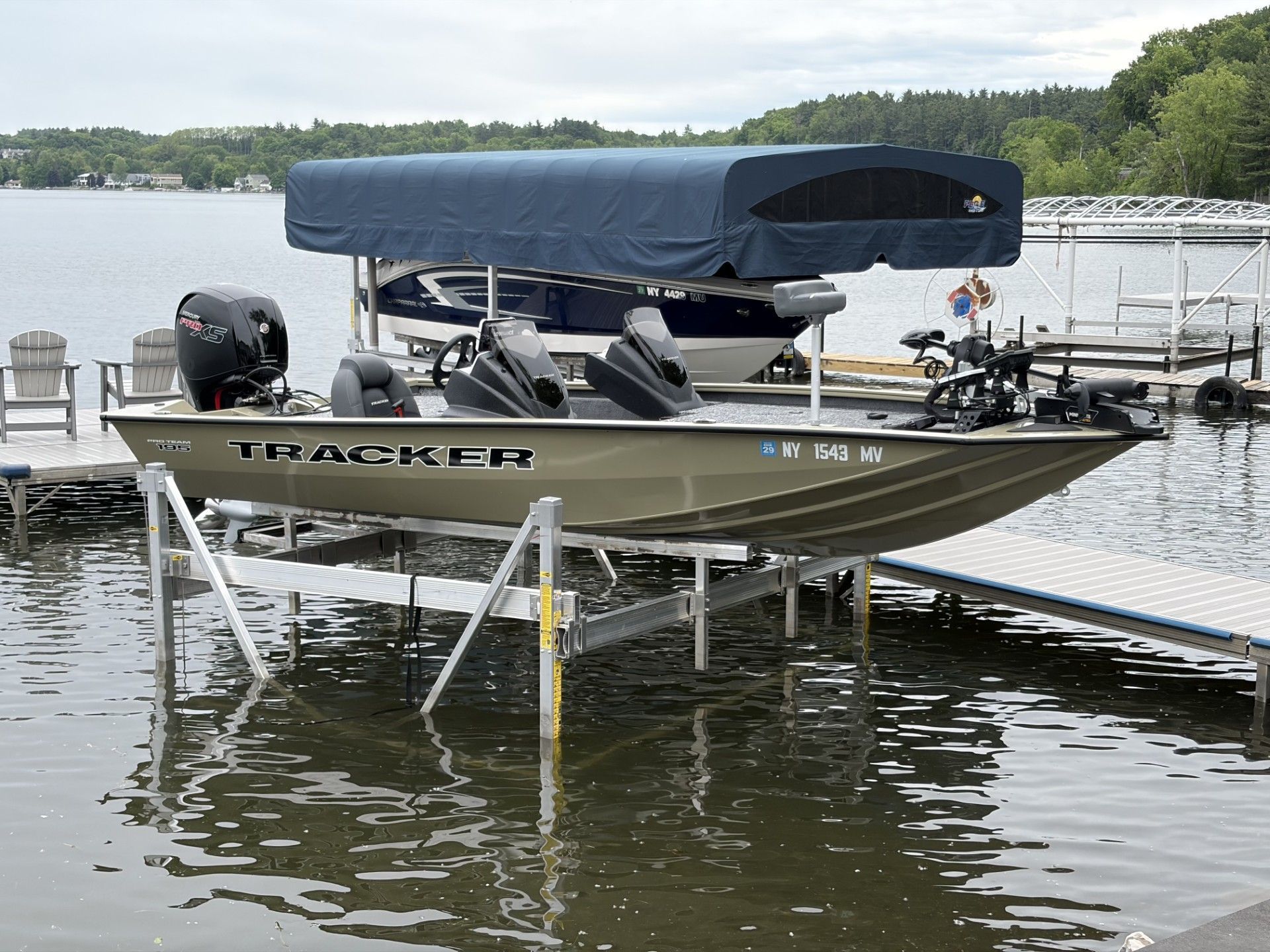Silver fishing boat with blue canopy docked on a lake beside a wooden pier