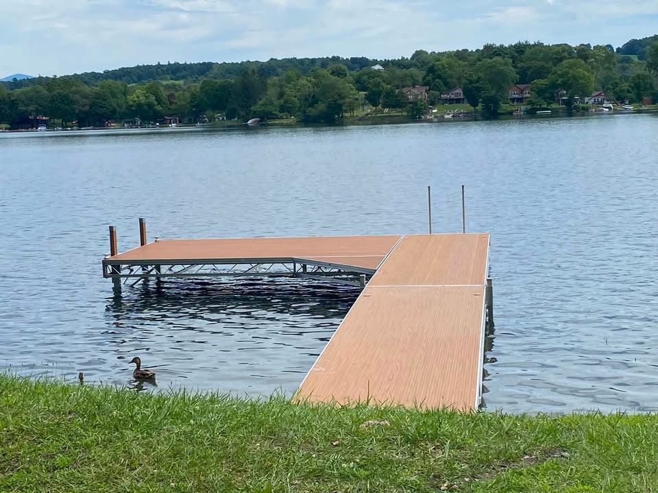 Wooden dock extends into a calm lake with a grassy shore in the foreground and trees across the water.