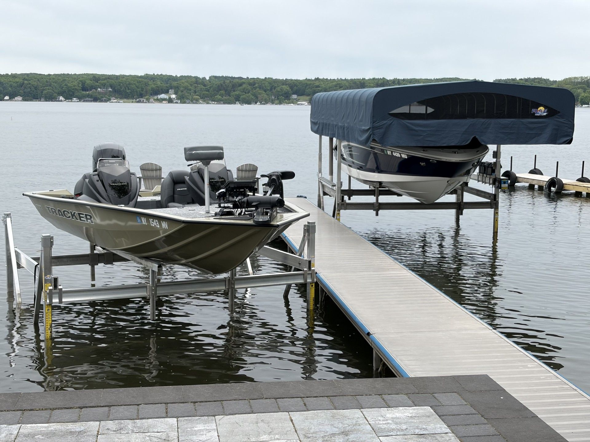 Two boats moored beside a dock on a calm lake, one covered and one open with motors attached
