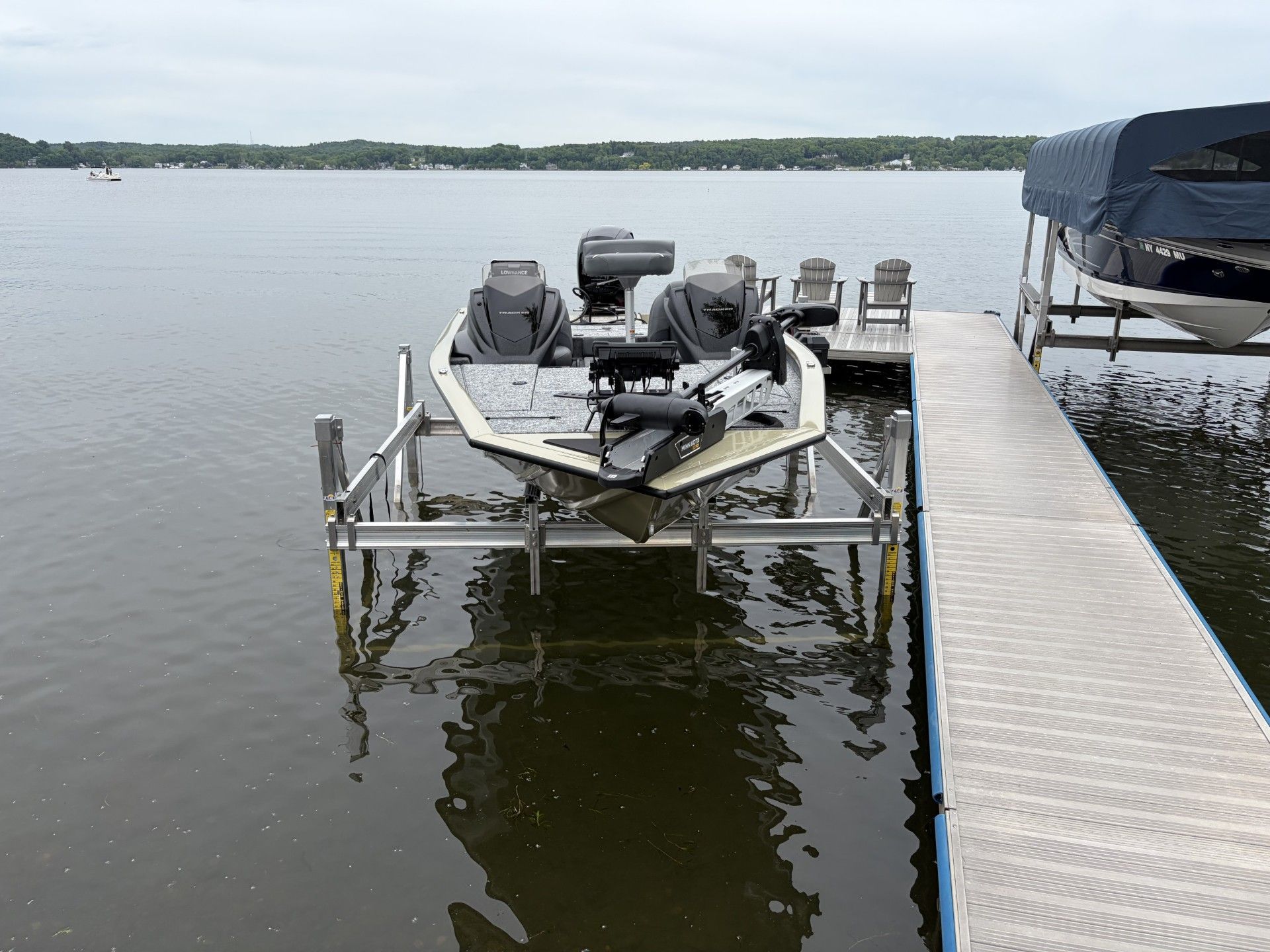 Small motorboat on a lift beside a dock on calm lake water under cloudy skies