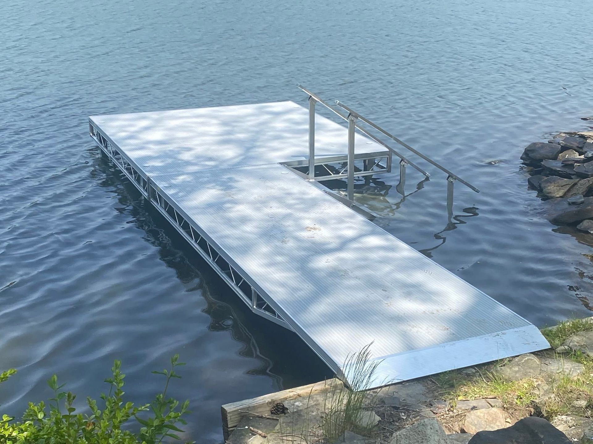 Floating dock on calm water with a small metal ladder and railings near the shore