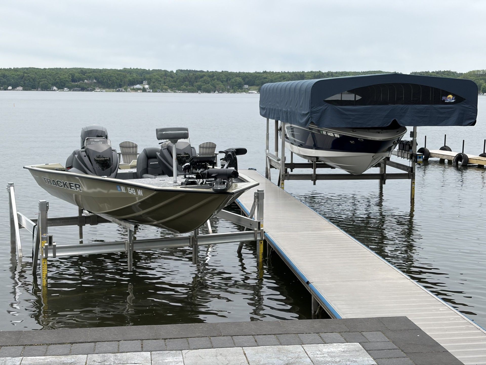 Fishing boat and covered speedboat docked at a lakeside pier on calm water.