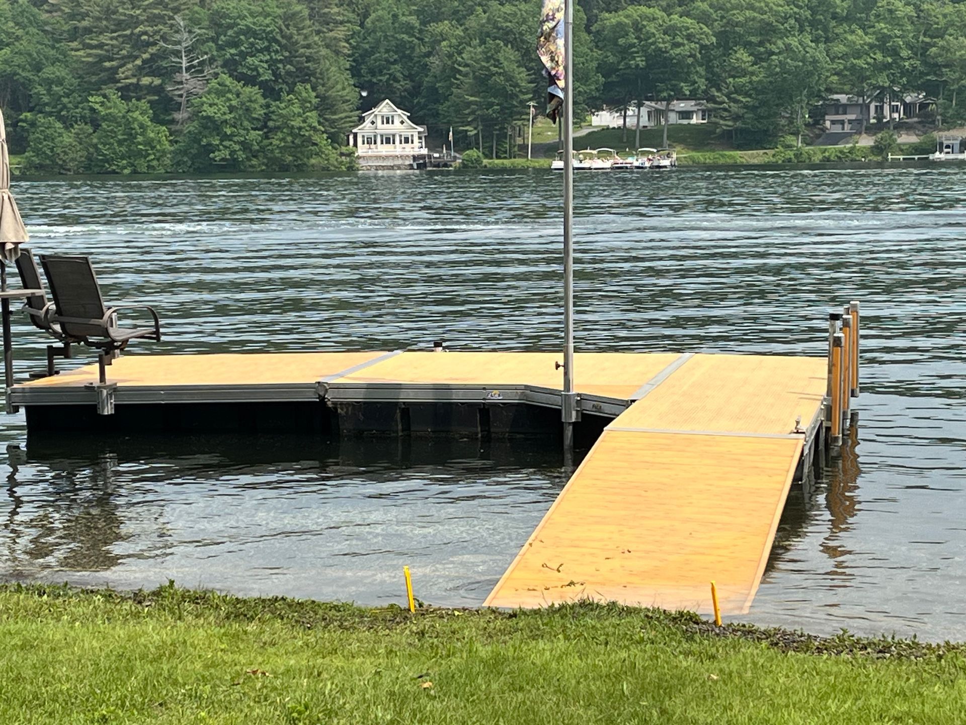 A floating yellow dock with a ramp leading to a grassy shore, overlooking a lake with a house in the distance.