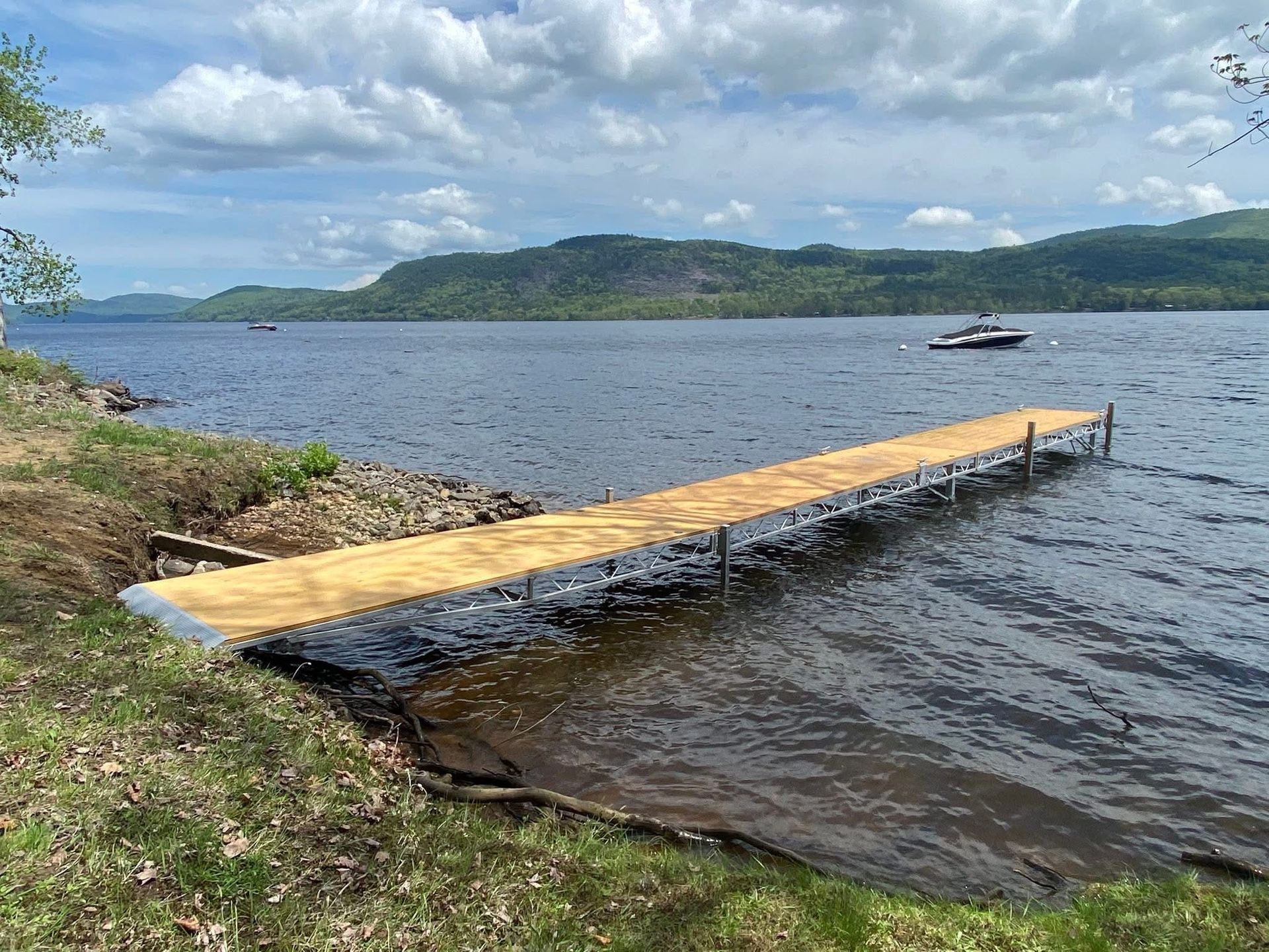 A wooden dock extending into a lake, with a mountain range in the distance on a cloudy day.