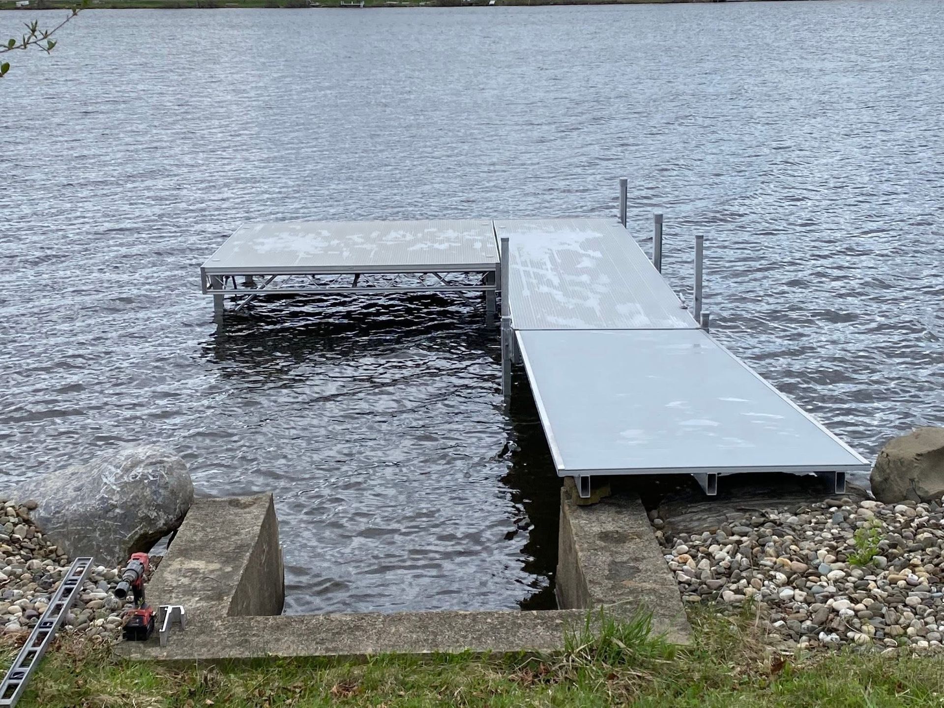 A dock with metal platforms extending into a body of water. Gray concrete and rocks line the shore.
