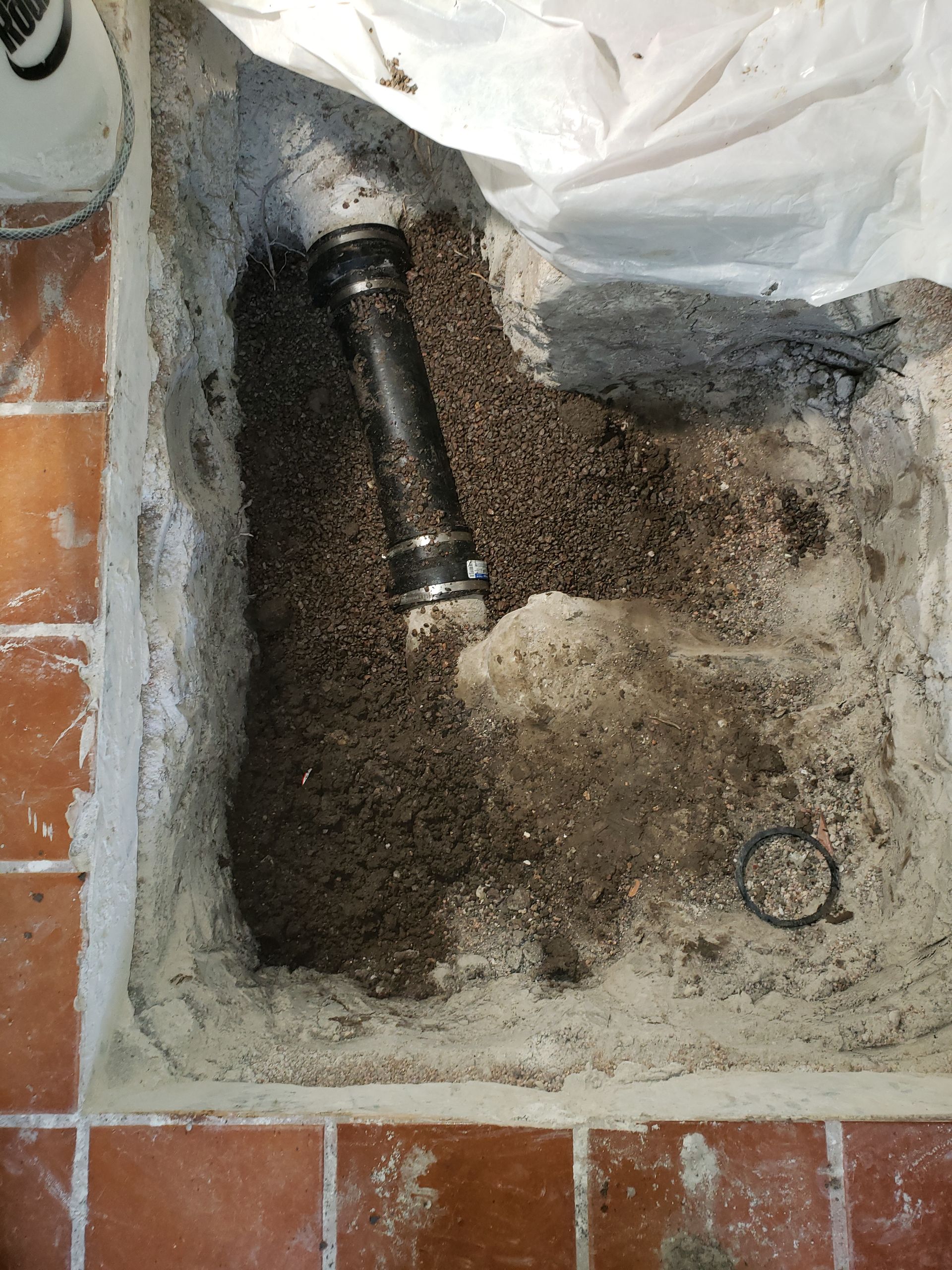 A hole in a tiled floor with a pipe, surrounded by gravel and cement.