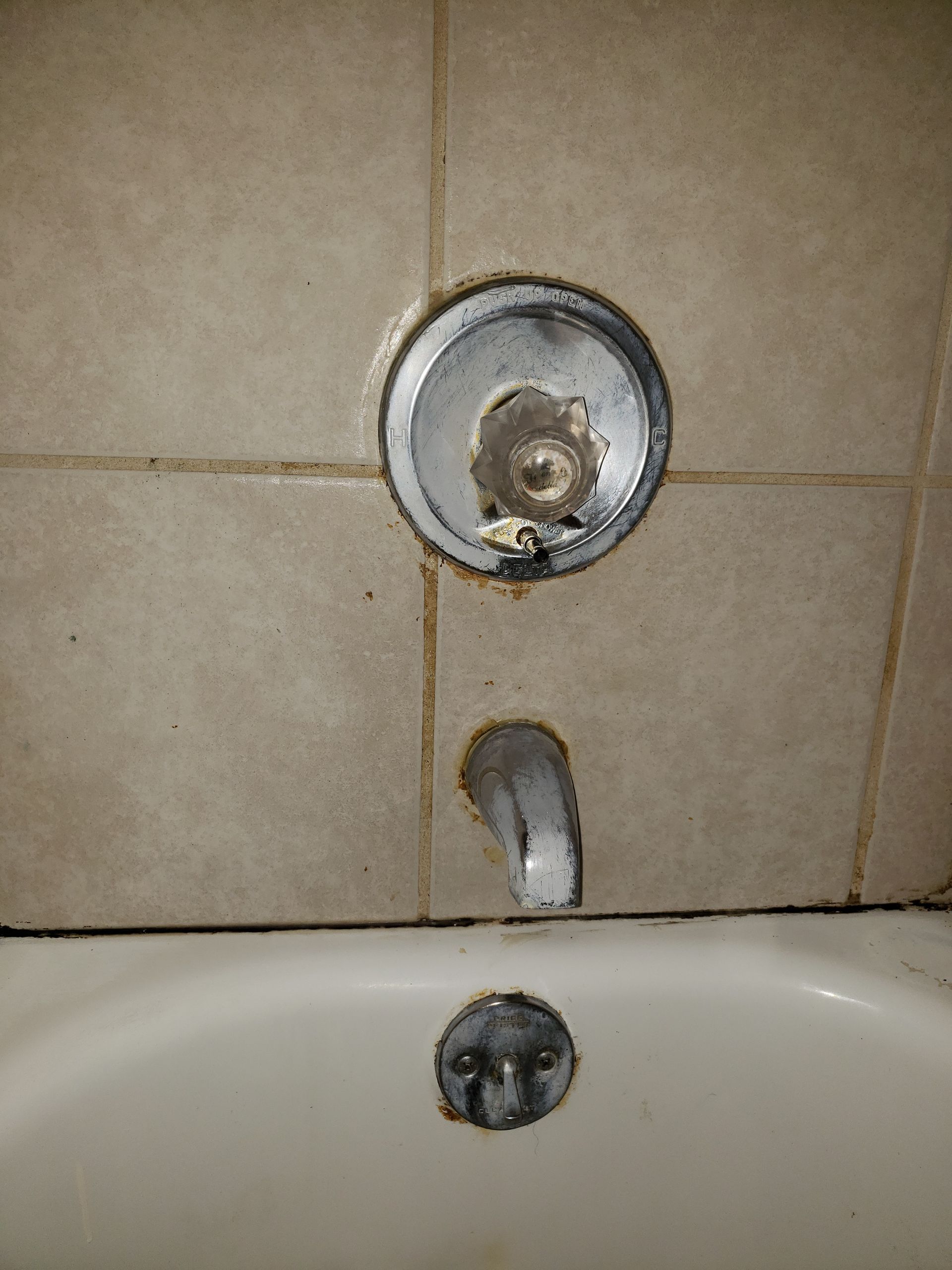 Shower faucet and tub spout, with mold around fixtures on beige tiled wall.