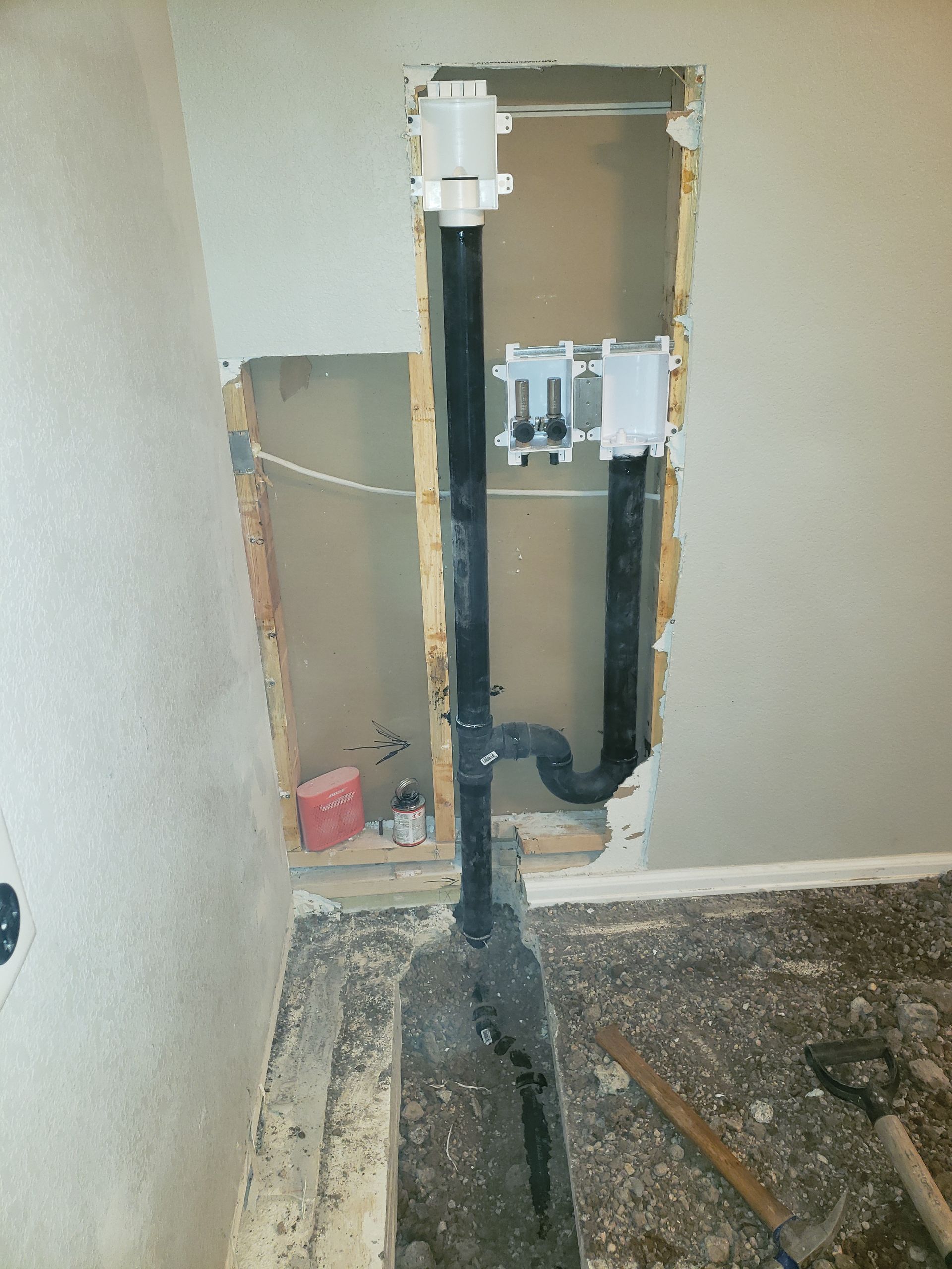 Plumbing rough-in with black drain pipes, a white valve, and electrical box in a wall cavity, near a concrete floor.