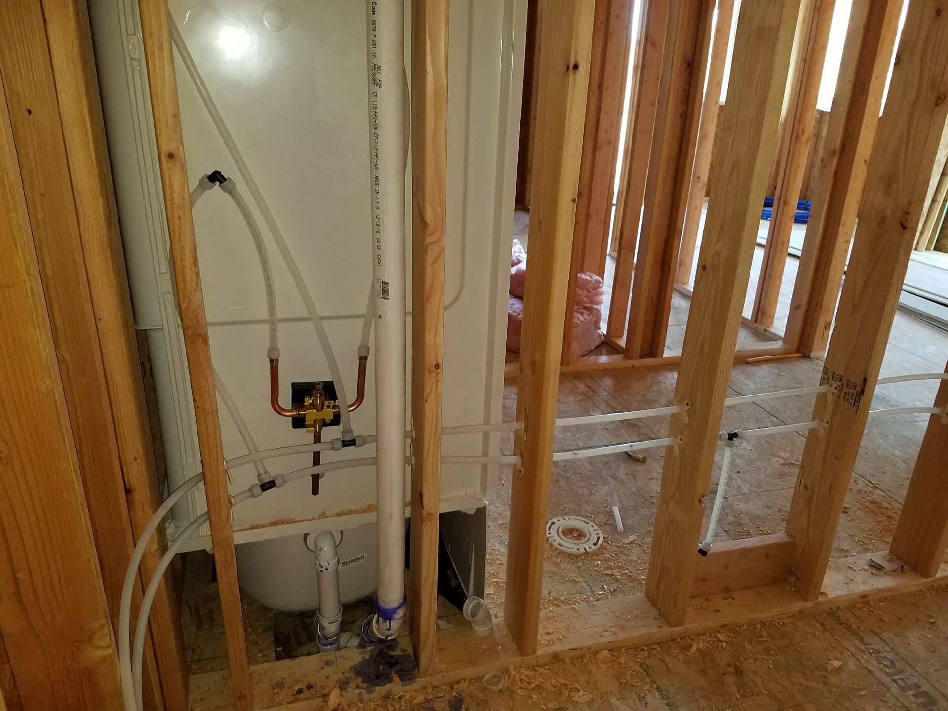Framed wall with a white water heater and plumbing. Interior of a building under construction.