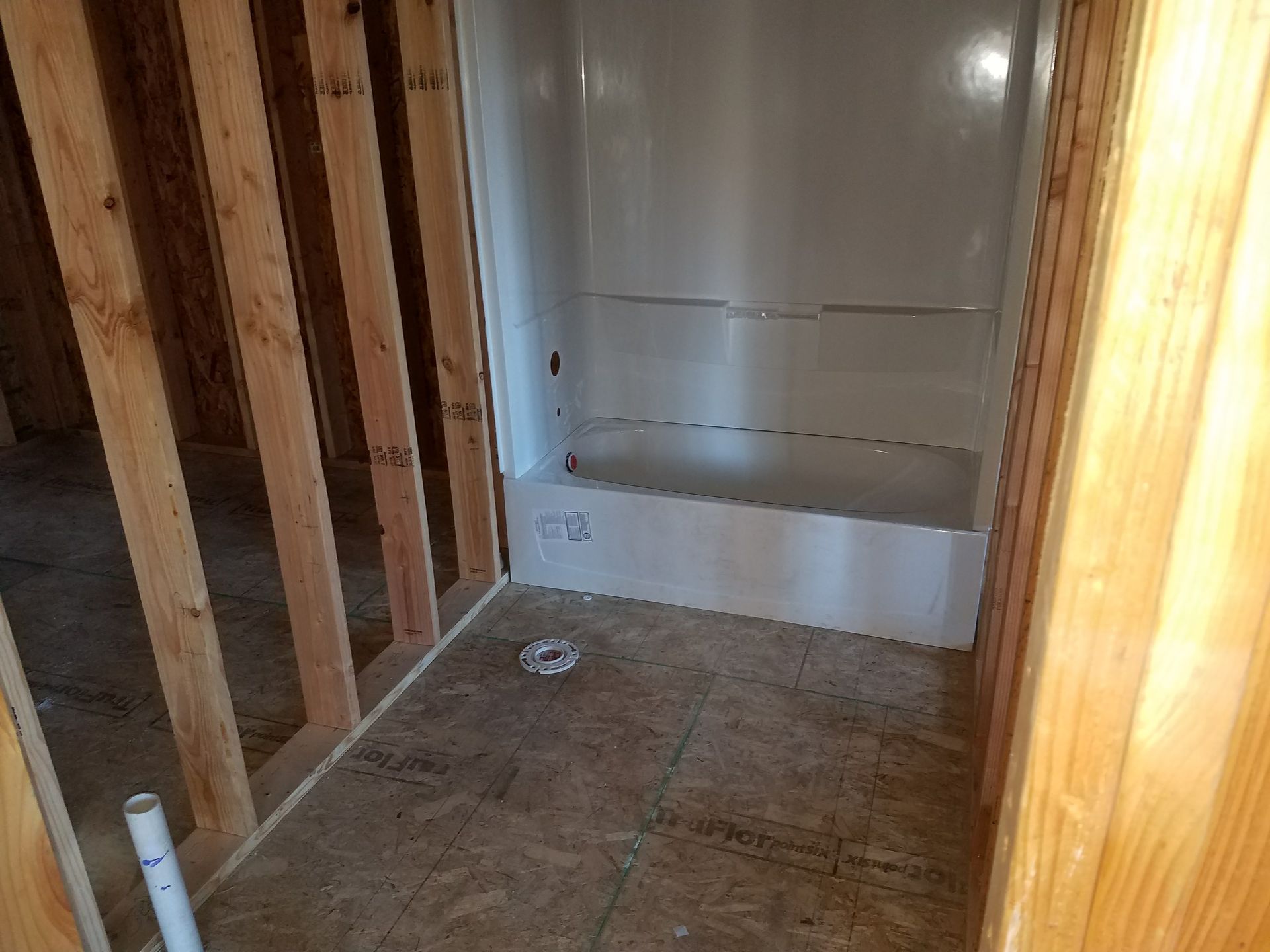 Bathroom under construction with a white bathtub unit, framed by wooden studs.