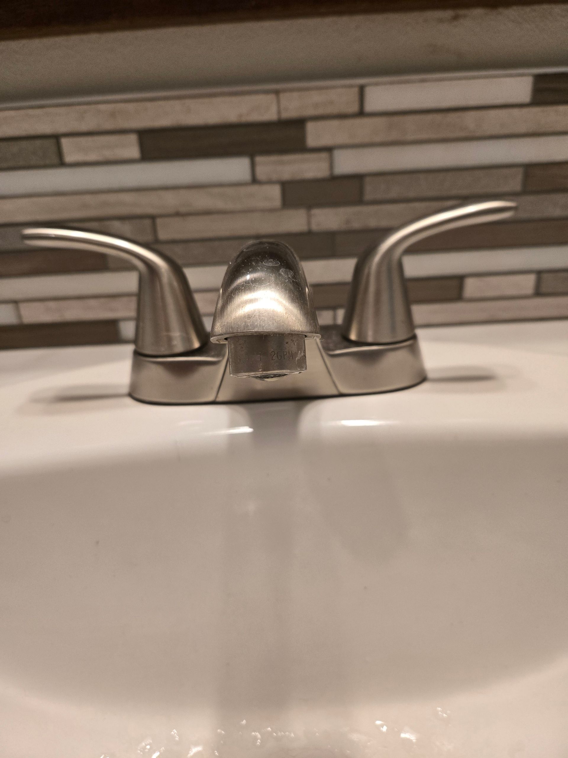 A bathroom sink with a faucet and a tiled wall behind it.