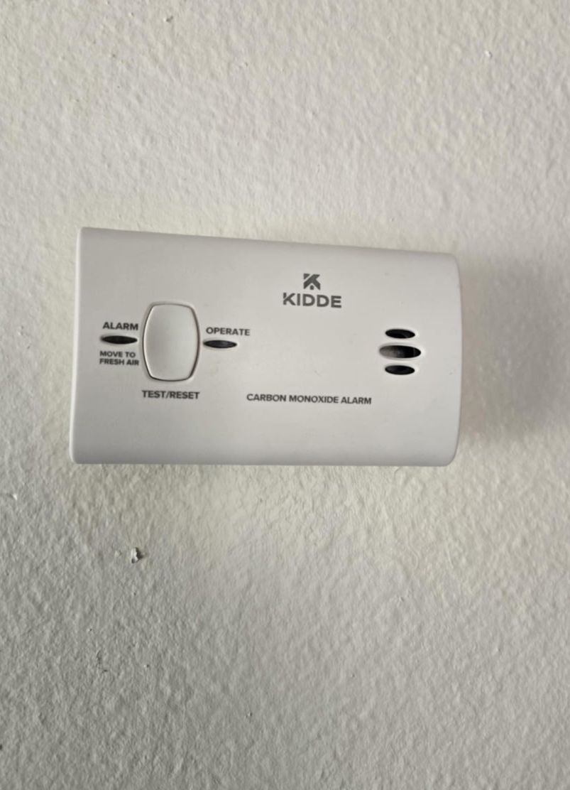 A white kidde smoke detector is mounted on a white wall