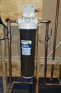 A water filter is attached to a copper pipe in a basement.