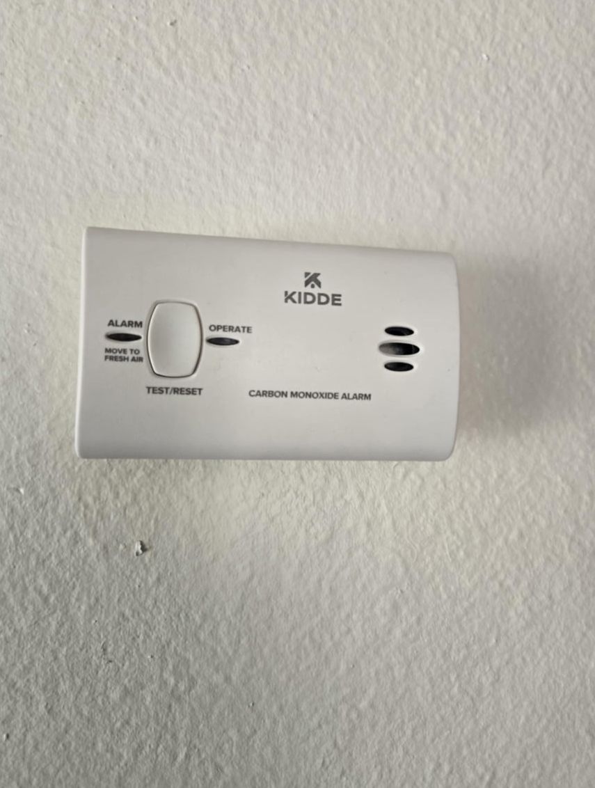 A white smoke detector is mounted on a white wall.