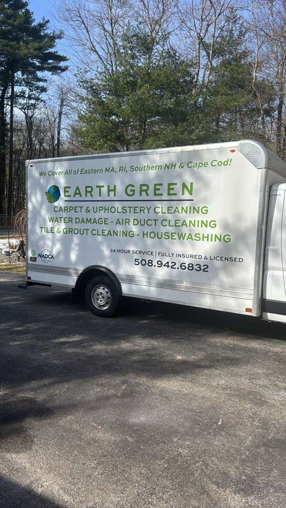 A white Earth Green service trailer parked on an asphalt driveway with trees in the background.