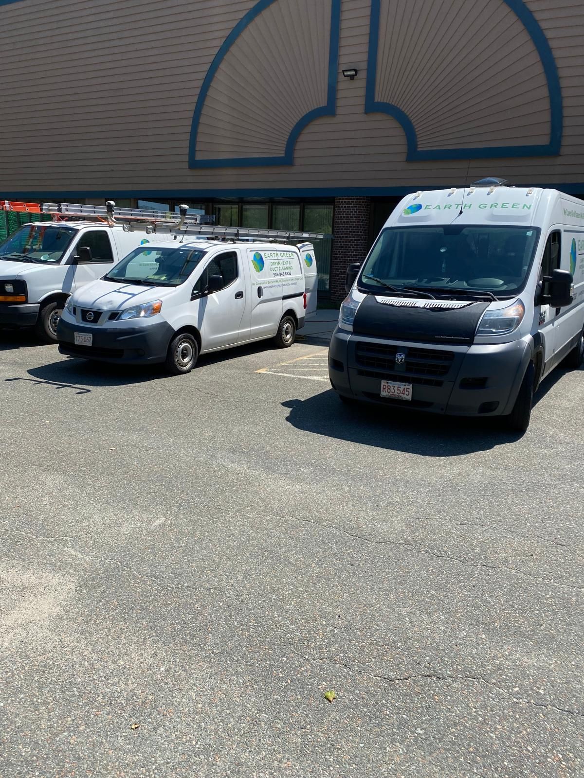 Three white work vans parked in a row on a gravel parking lot in front of a building with a large curved architectural arc.