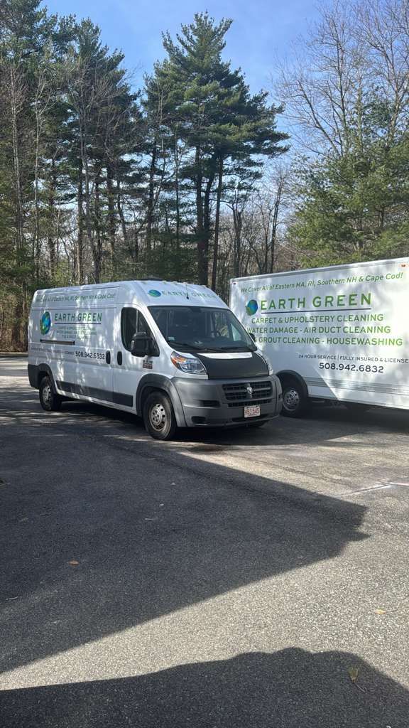 Two white Earth Green vans parked on an asphalt lot in front of trees under a clear blue sky.