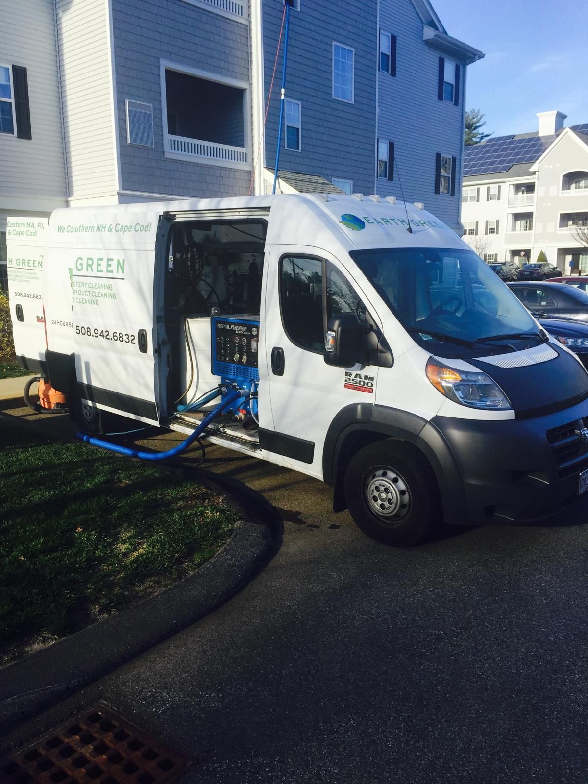 A white work van with open side doors, parked on an asphalt driveway next to a multi-story blue apartment building.