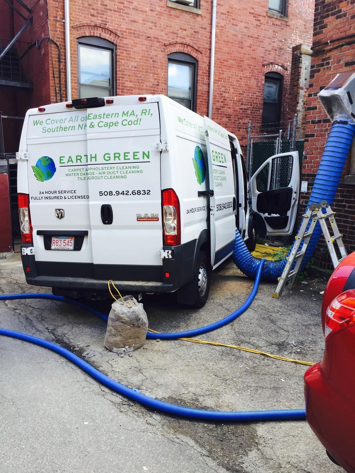 An Earth Green restoration van parked in an alley, connected to a building by a large blue industrial hose.