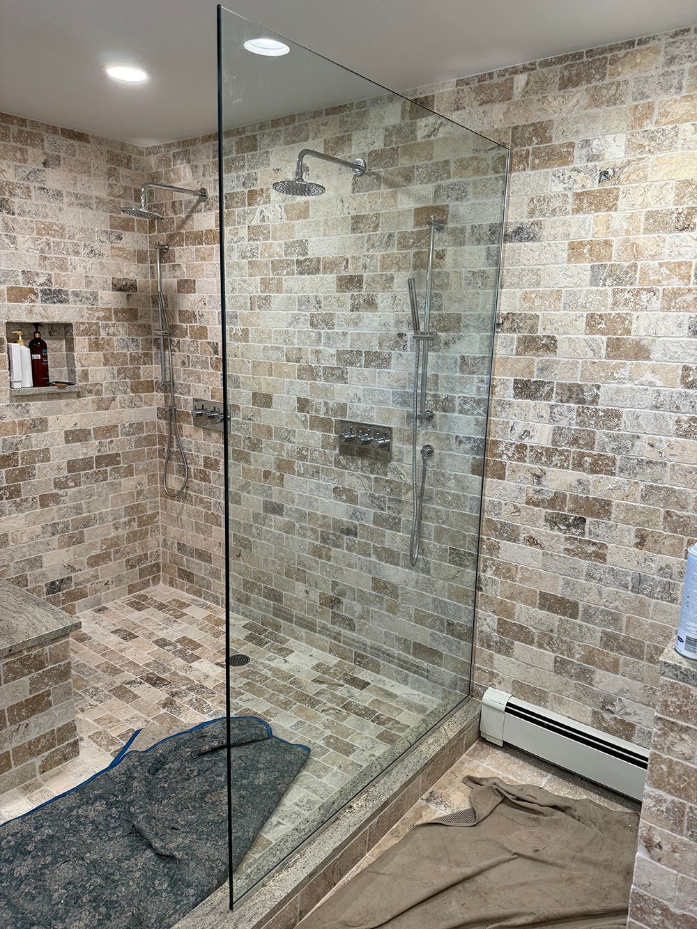 Glass shower enclosure in a tiled bathroom with stone-look walls and floor.