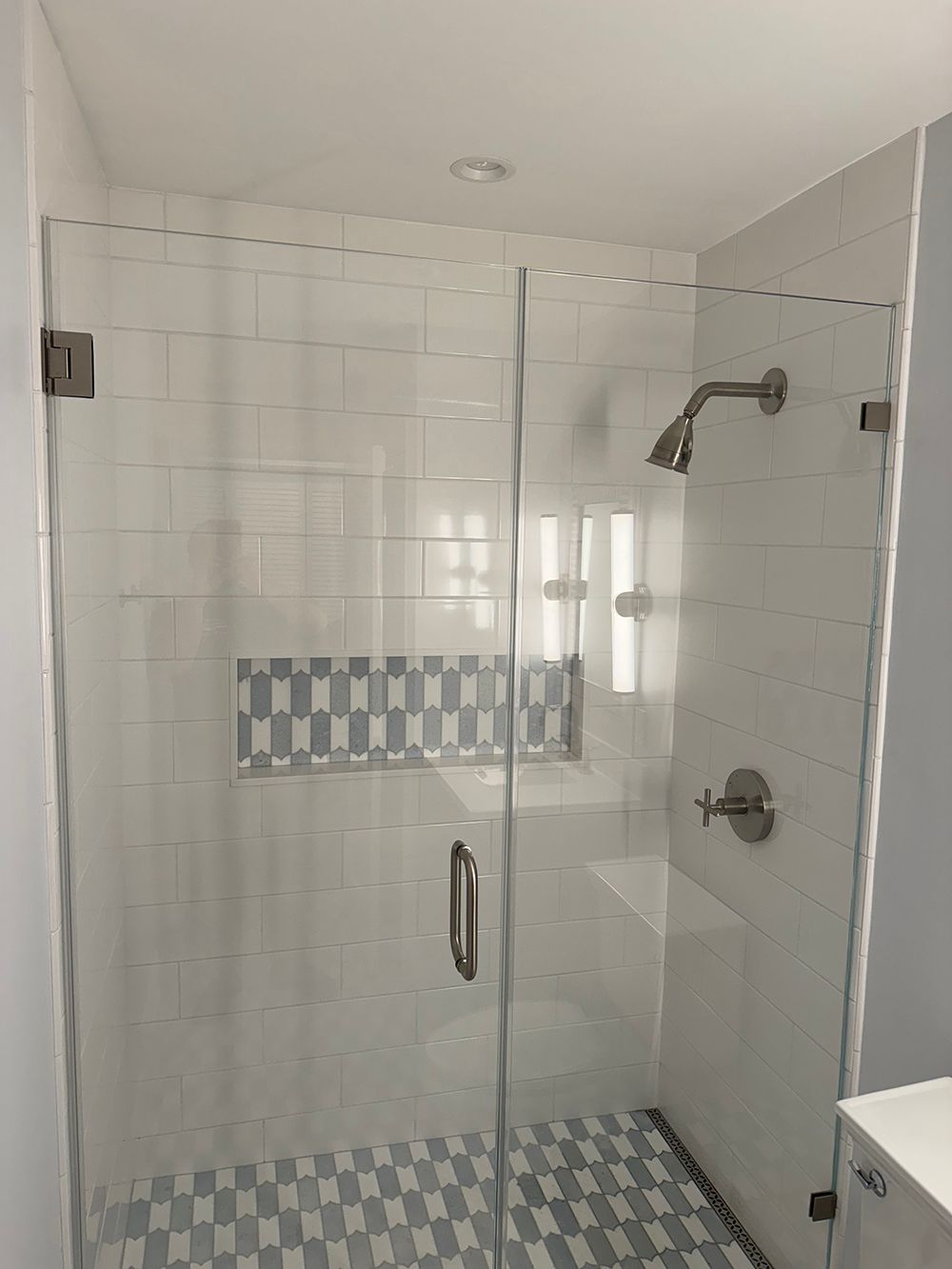 Glass shower stall with white tile walls and blue patterned accent tiles and floor.