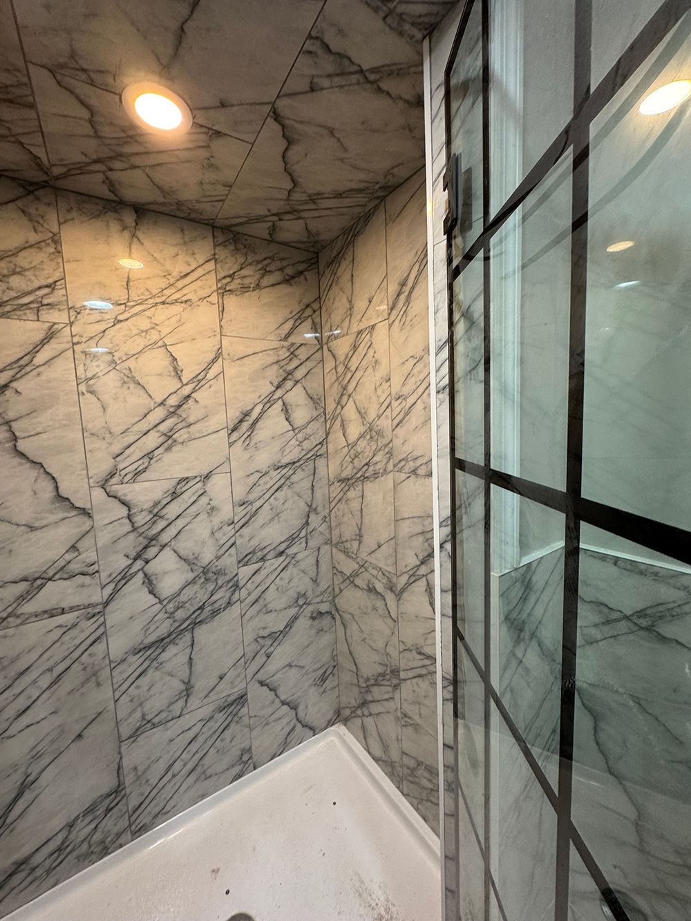 Marble-tiled shower corner with glass door and ceiling light