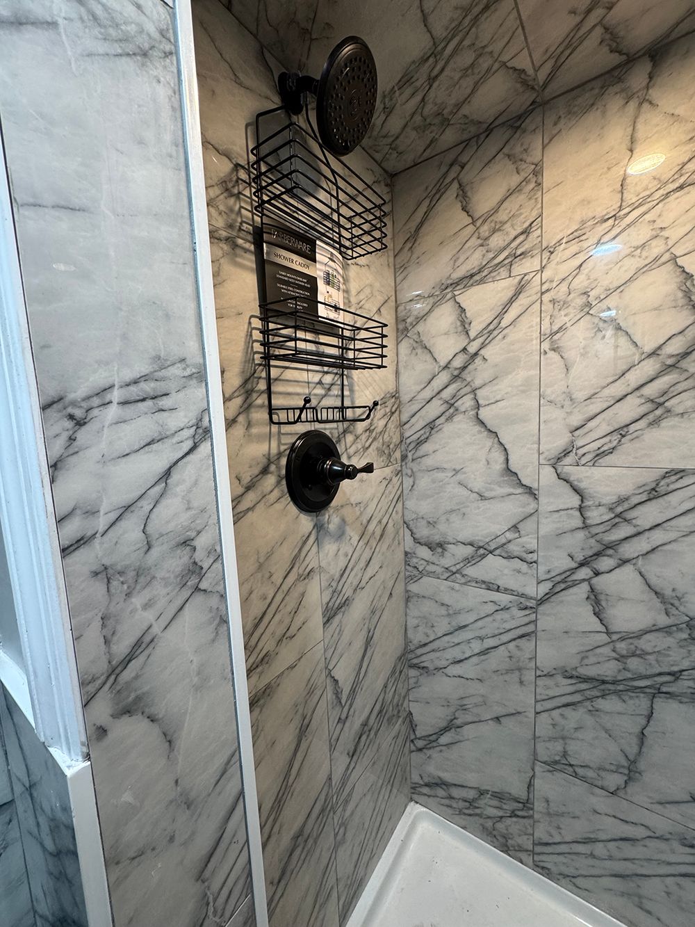 Wall-mounted black wire shower caddy and suction basket on marble-tile bathroom wall.