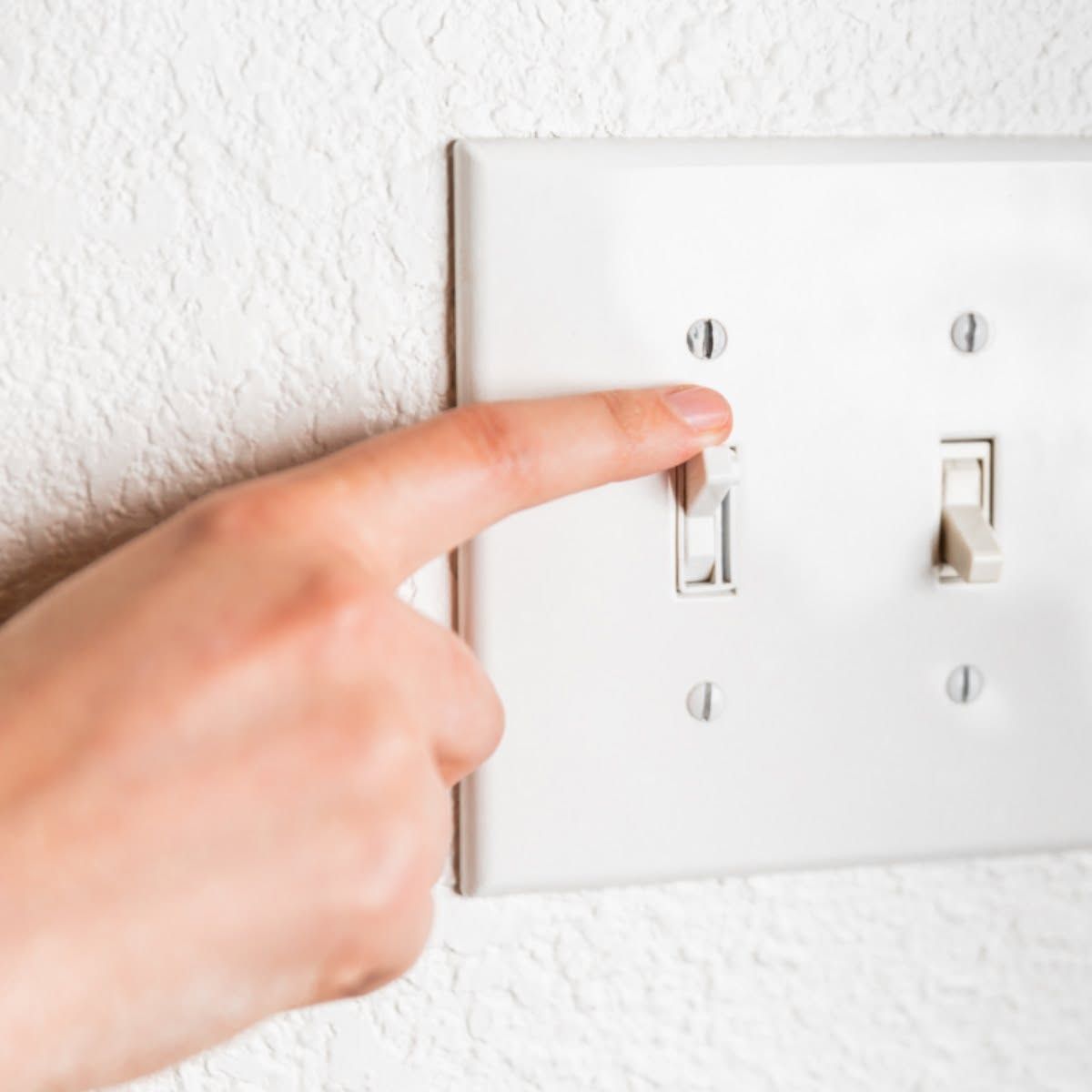 A person is pressing a light switch with their finger.