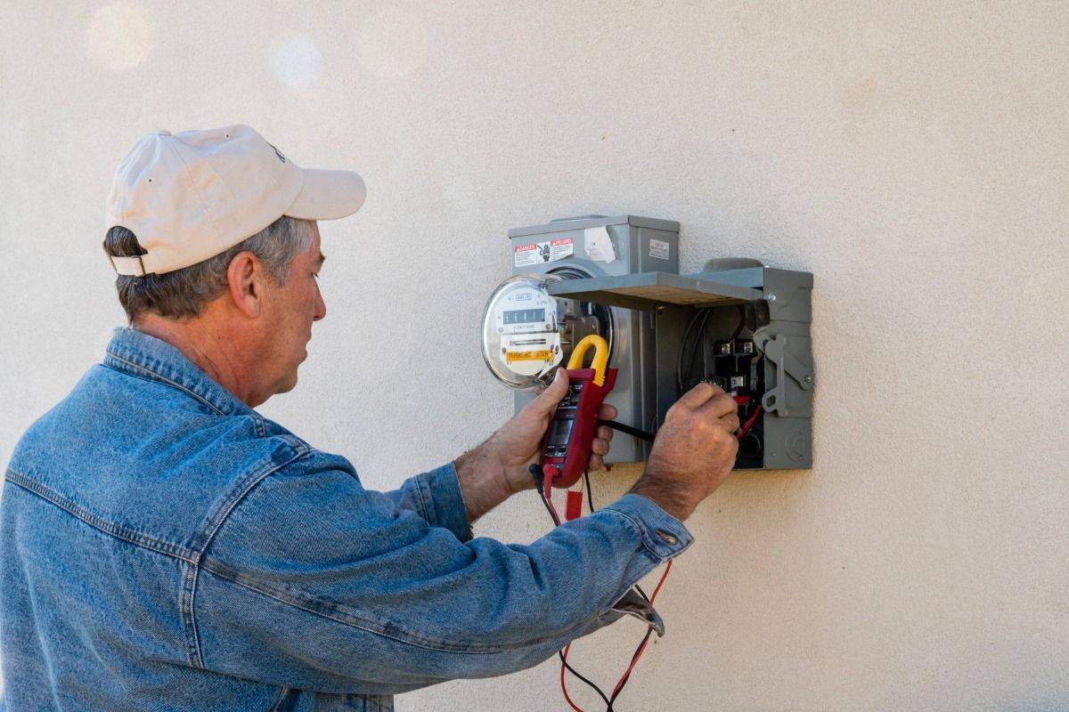 A man is working on an electrical box on a wall.