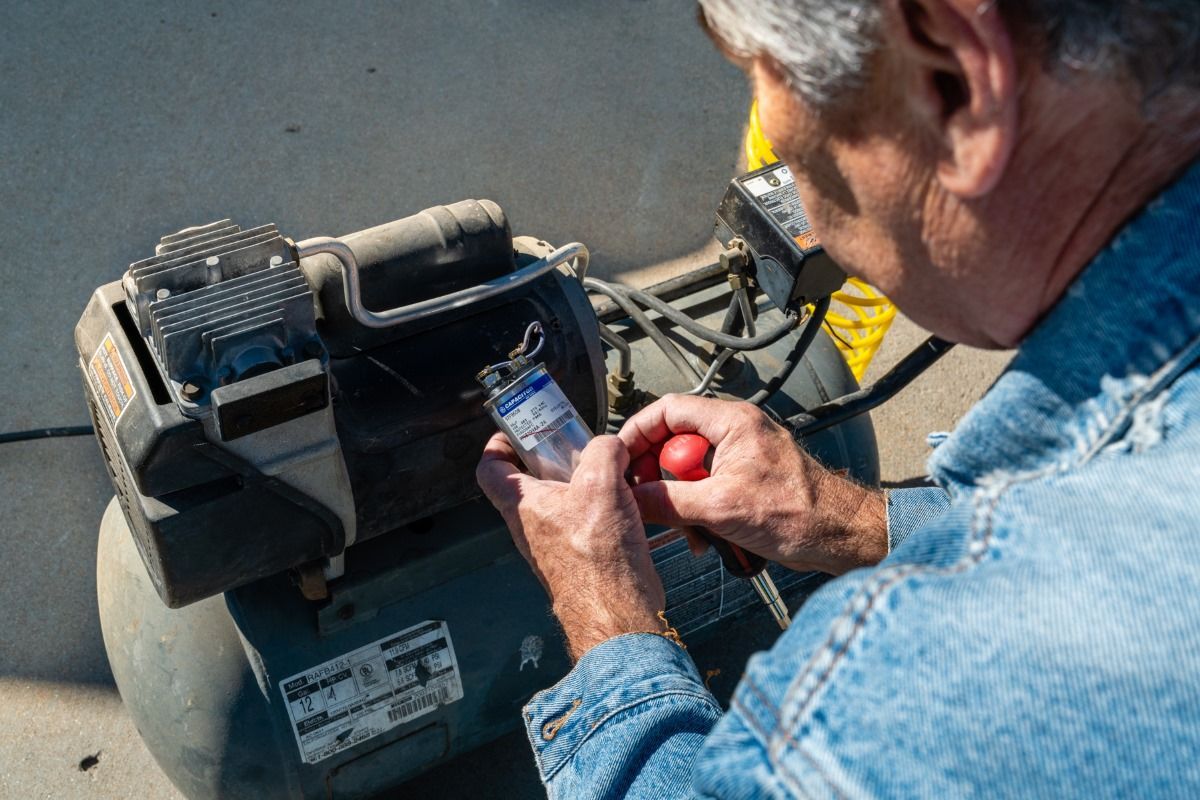 A man is fixing an air compressor with a screwdriver.