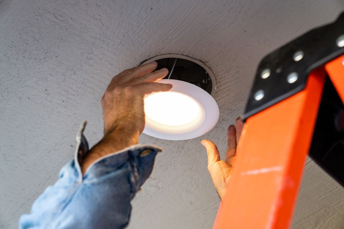 A man is standing on a ladder installing a light on the ceiling.