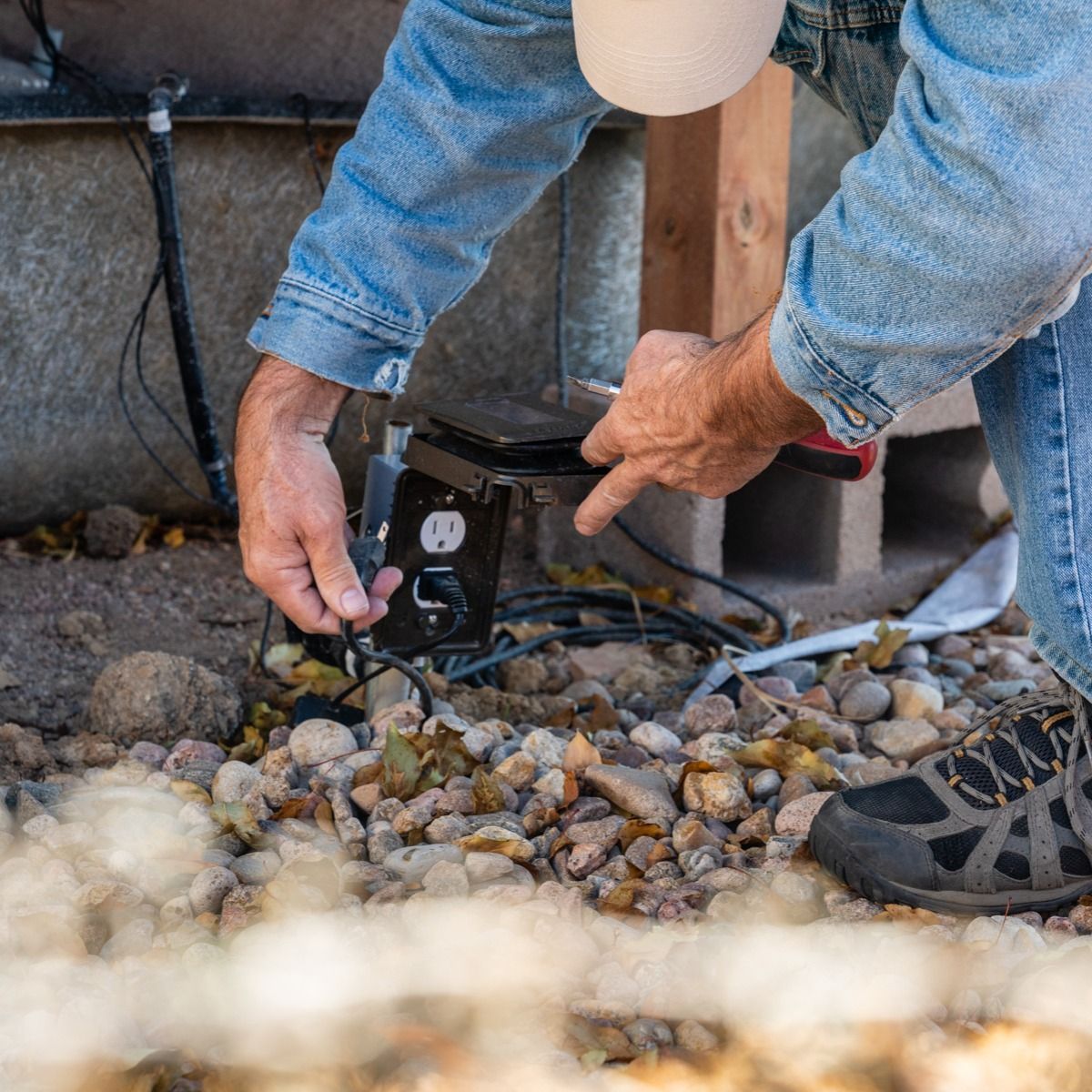 A man is plugging a cord into an outlet on the ground.