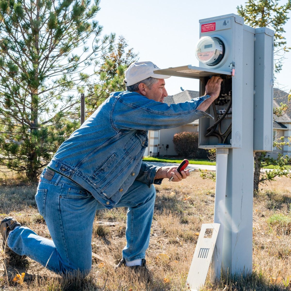 A man in a denim jacket is working on an electrical box