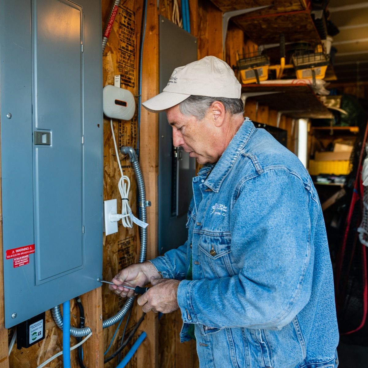A man in a denim jacket is working on an electrical box