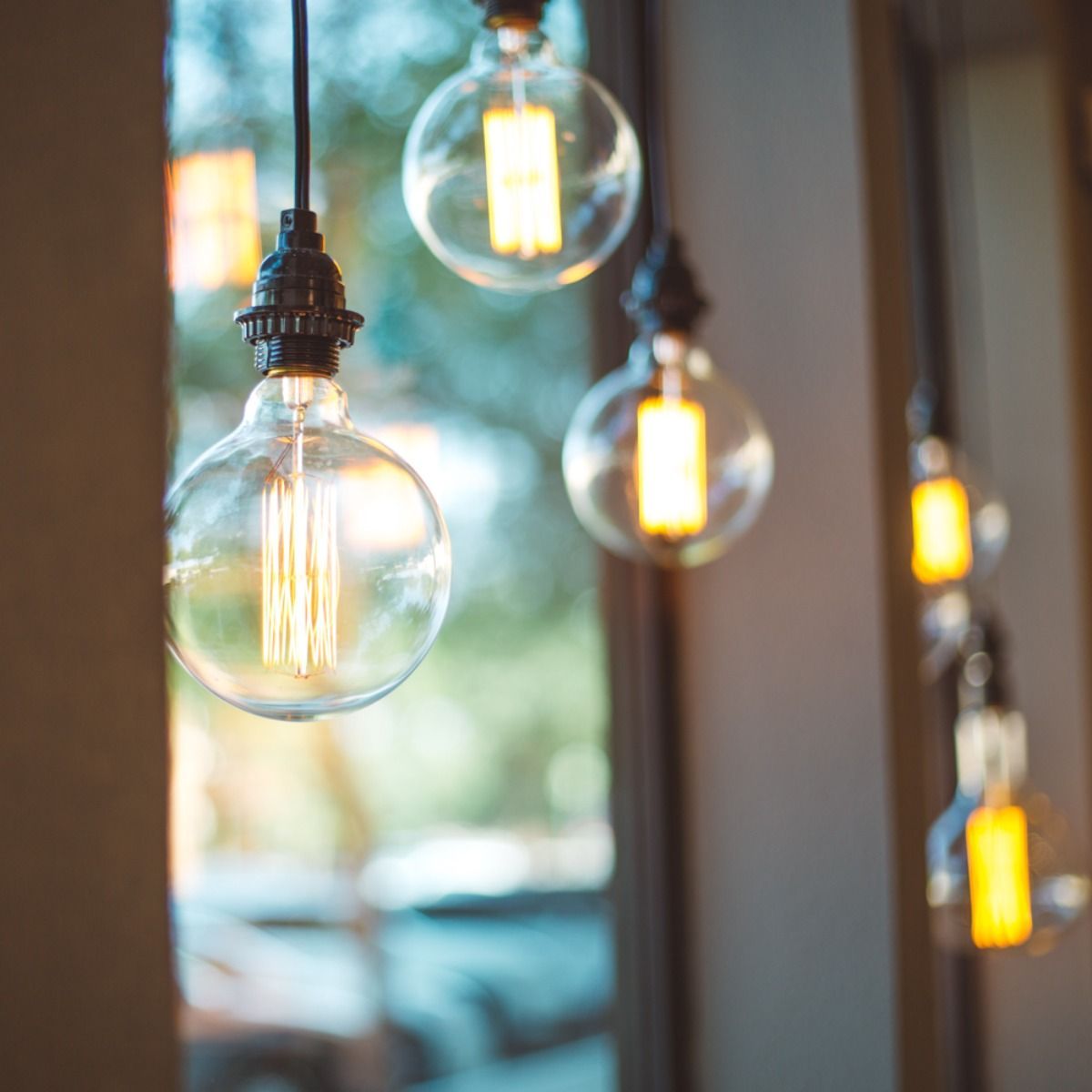 A bunch of light bulbs hanging from the ceiling in front of a window.