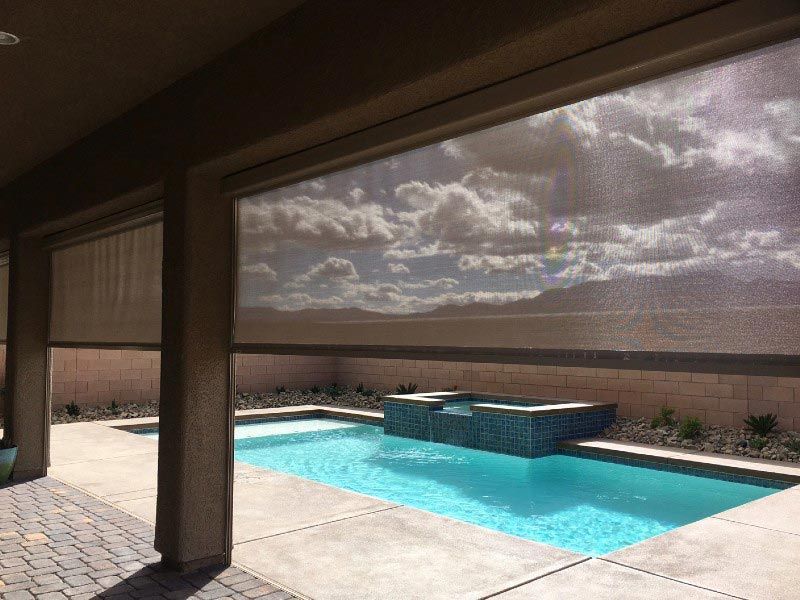 A swimming pool is behind a screened in porch with a view of the sky.
