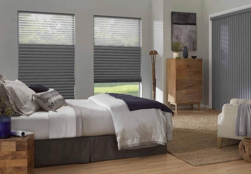 A bedroom with a bed , dresser , chair and window shades.