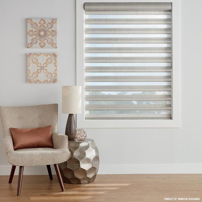 A living room with a chair , table , lamp and window with blinds.