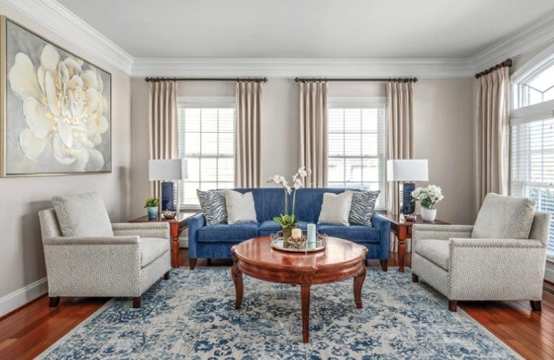 A living room with a blue couch , two chairs , a coffee table and a rug.