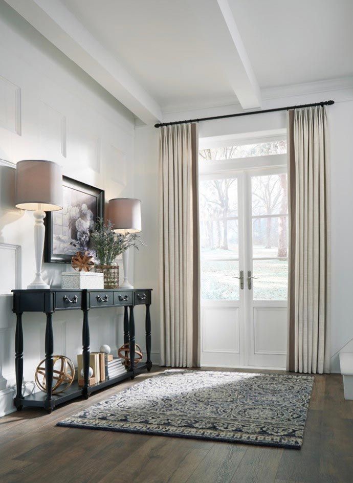 A living room with a table , lamps , curtains and a rug.