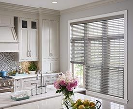A kitchen with white cabinets , a sink , and a window with blinds.