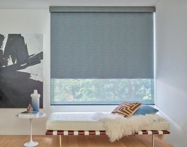 A bed is sitting in front of a window with blue blinds.