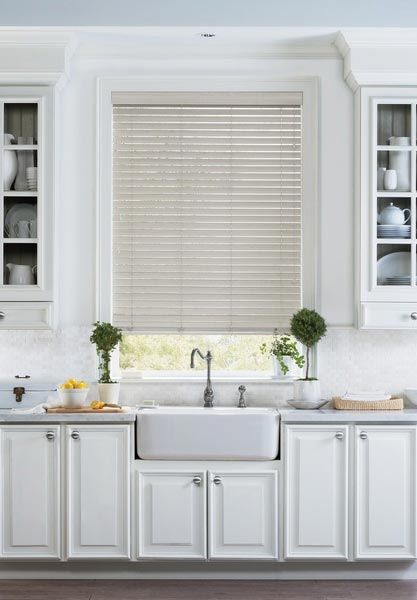 A kitchen with white cabinets , a sink , and a window with blinds.