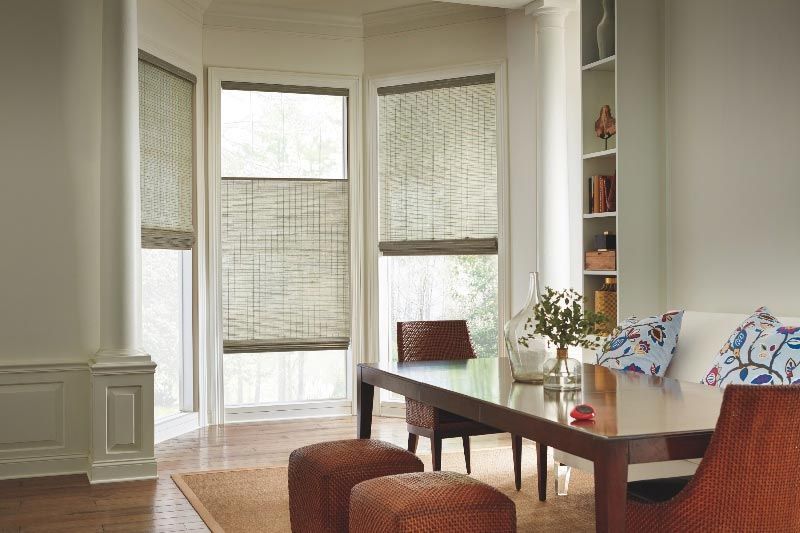 A living room with a table , chairs , ottomans and roman shades.