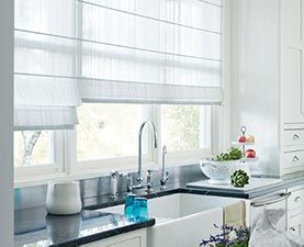 A kitchen with a sink and a window with roman shades.